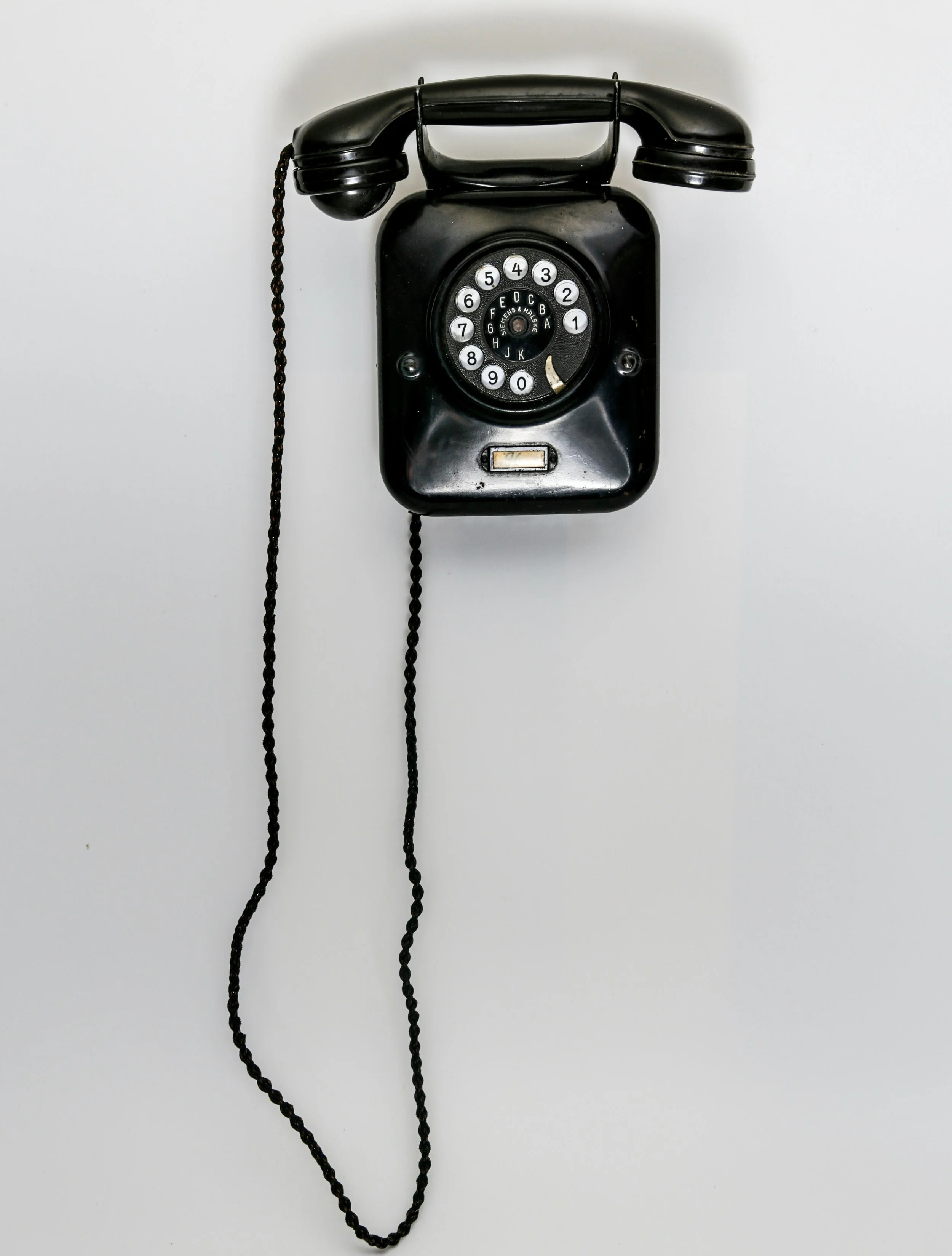 Black vintage rotary telephone mounted on a plain white wall.