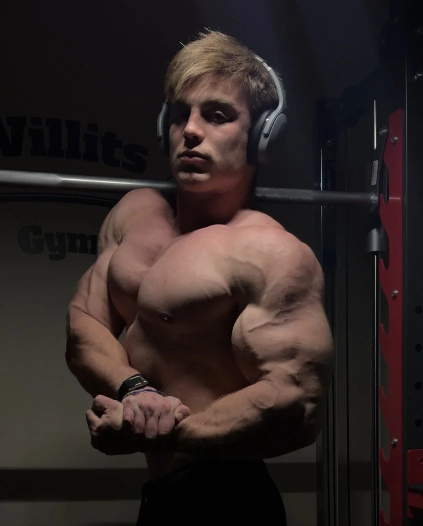 Bodybuilder posing in a commercial gym while wearing headphones, highlighting physique built through consistent training and nutrition coaching.