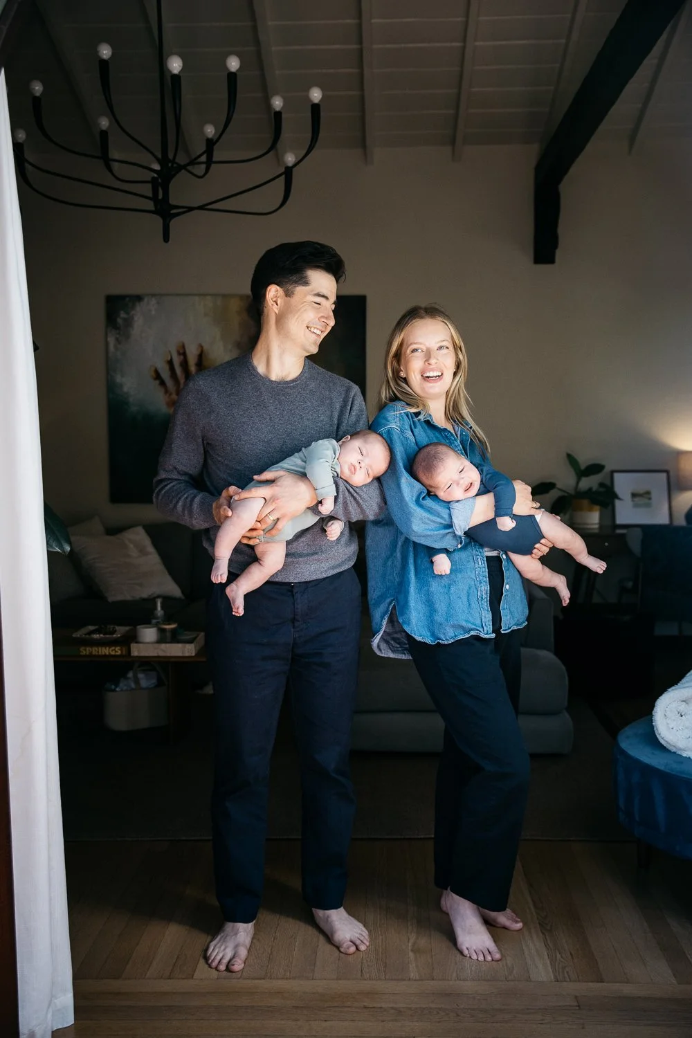 Parents stand in doorway, smiling at each other and holding newborn twins, shot in Piedmont during newborn photo session.