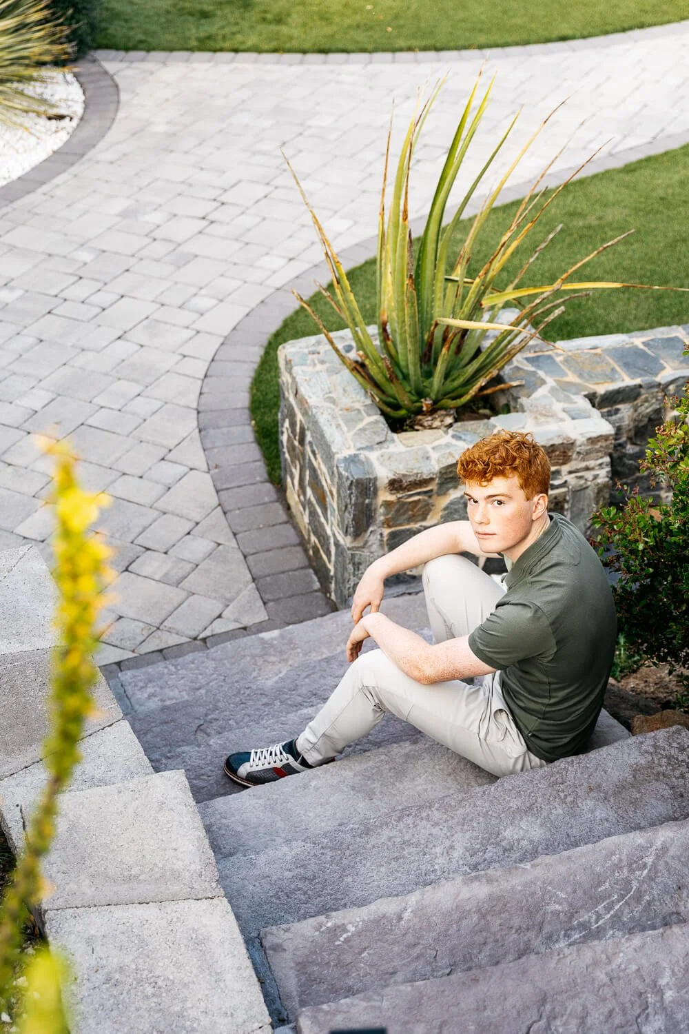 Senior portrait of redheaded teen in backyard with gray stone steps and landscaping, shot in Orinda, CA.