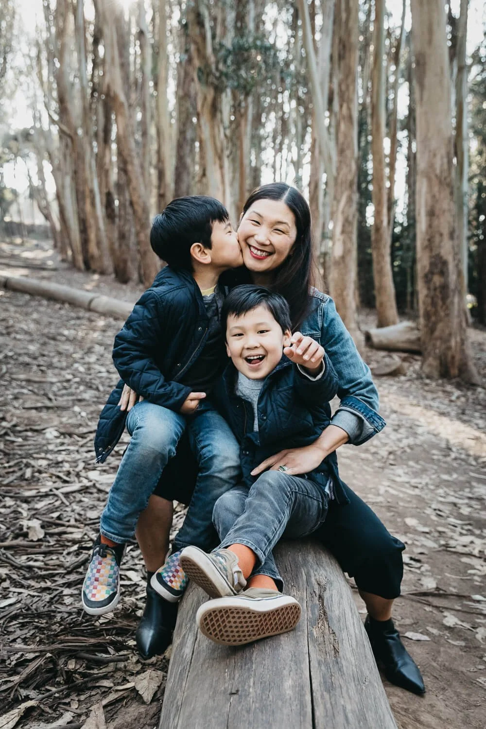 Asian mother with young twin boys sits on a log in the Presidio while her sons hug and kiss her. The kids are moving and playing, but the mother looks at the camera, giving the photo a good mix of candid moment and posed portrait.