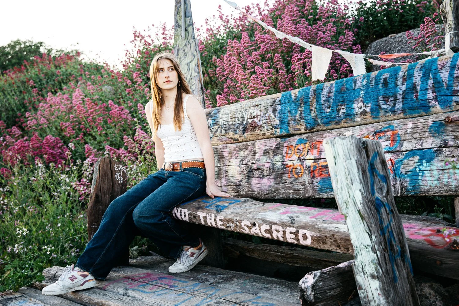 Senior girl sits on bench amongst wildflowers at the Albany Bulb.