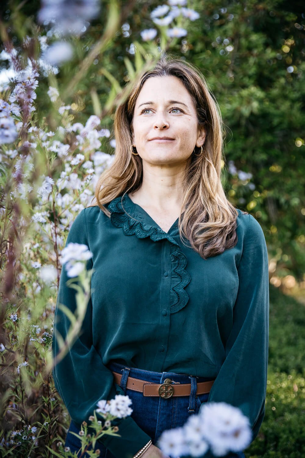 Woman in green silk blouse stands among purple flowers at Blake Gardens in Berkeley, CA.