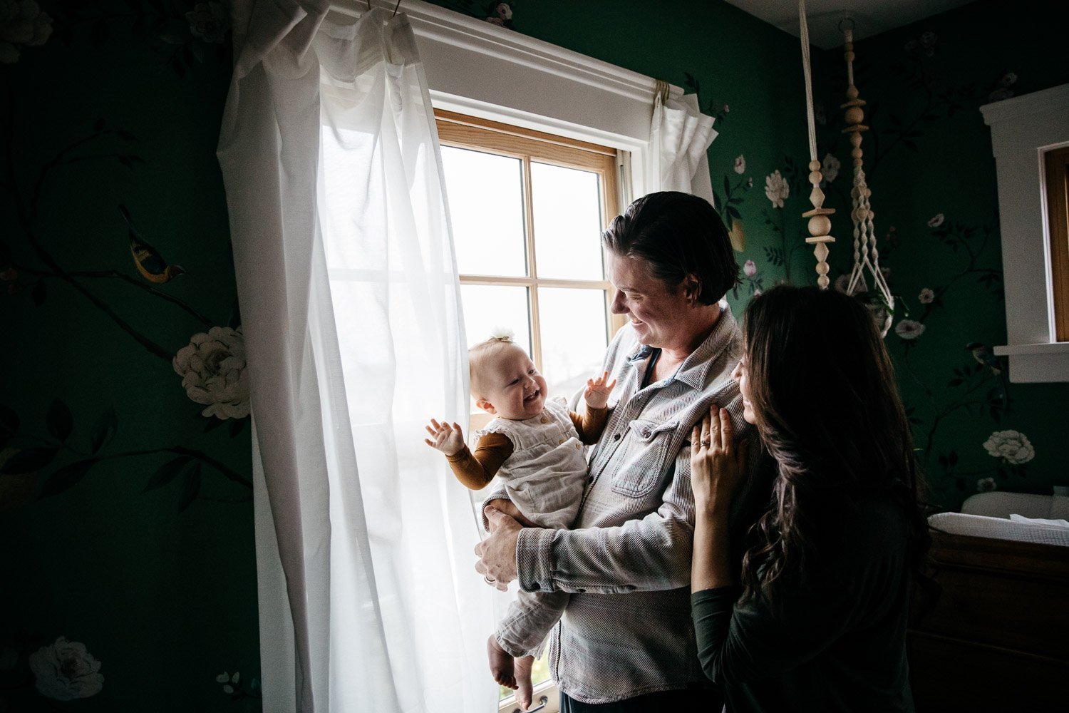  family photograph of mom, dad, and baby at home near wondow with soft light and fun wallpaper, shot in Berkeley by family photographer Allison Busch Photography 
