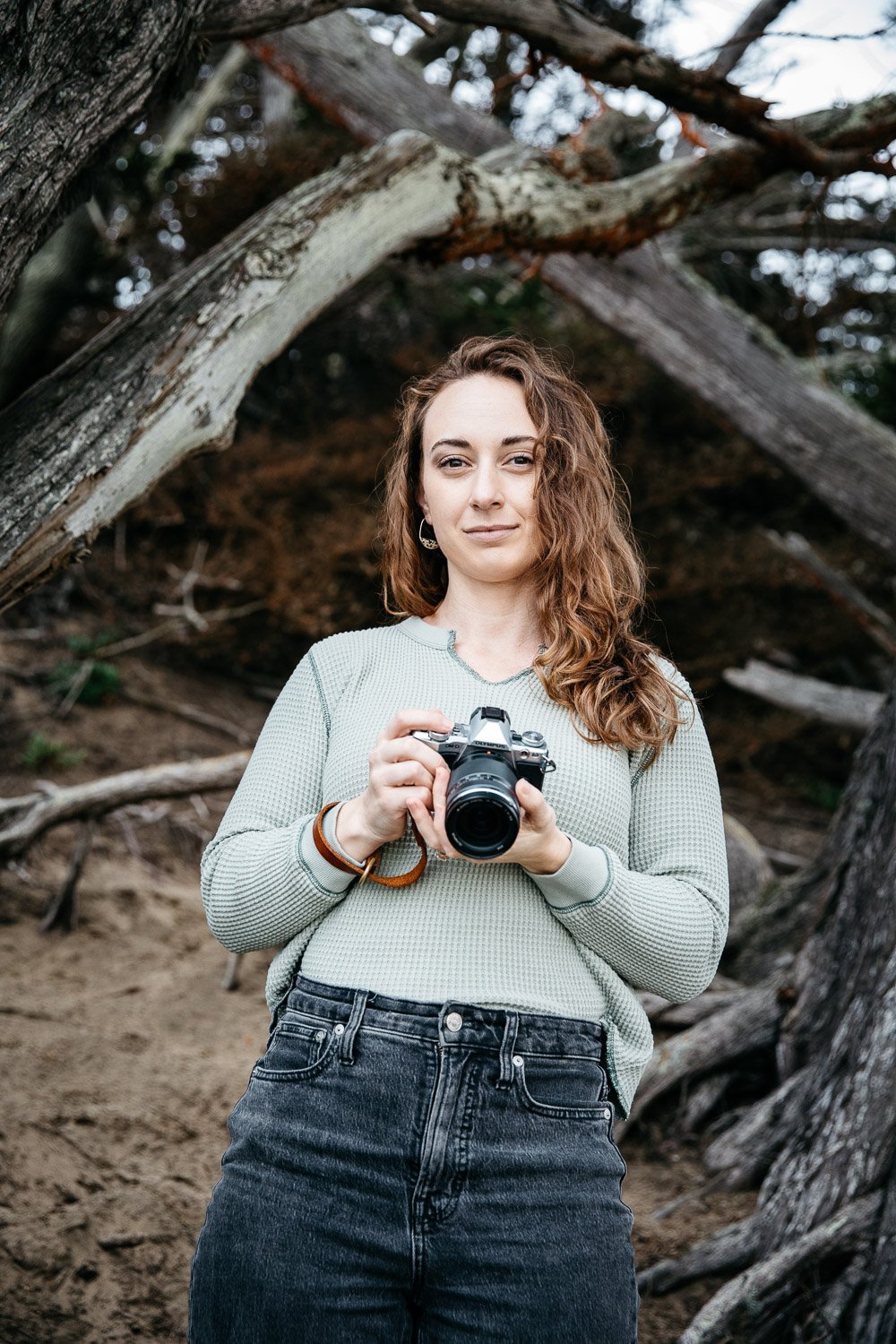  brand portrait of photographer Toni Toscano holding her Olympus camera and large trees behind her, shot at Baker Beach in San Francisco by brand photographer Allison Busch Photography 
