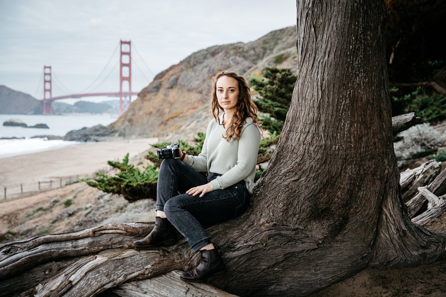  brand portrait of photographer Toni Toscano holding her Olympus camera and large trees behind her, shot at Baker Beach in San Francisco by brand photographer Allison Busch Photography 