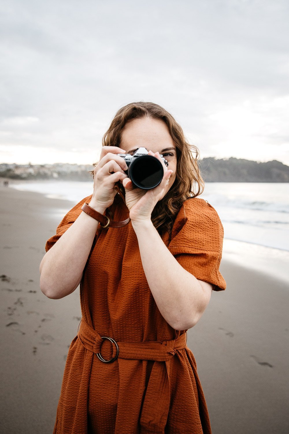  brand portrait of photographer Toni Toscano holding her Olympus camera with the ocean behind her, shot at Baker Beach in San Francisco by brand photographer Allison Busch Photography 