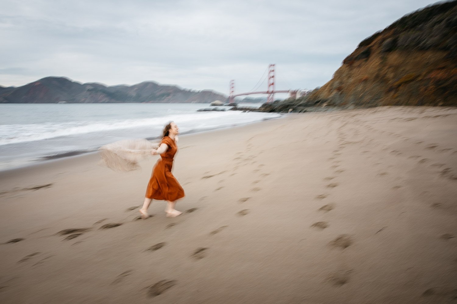  brand portrait of photographer Toni Toscano running with scarf in the wind and the Golden gate Bridge behind her, shot at Baker Beach in San Francisco by brand photographer Allison Busch Photography 