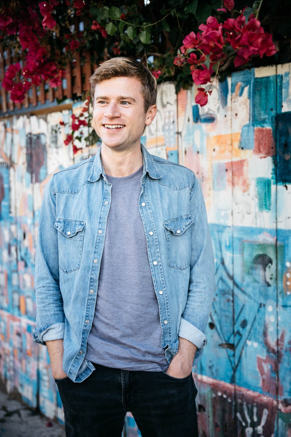 Man in blue shirt stands smiling in front of colorful mural in Balmy Alley, San Francisco.