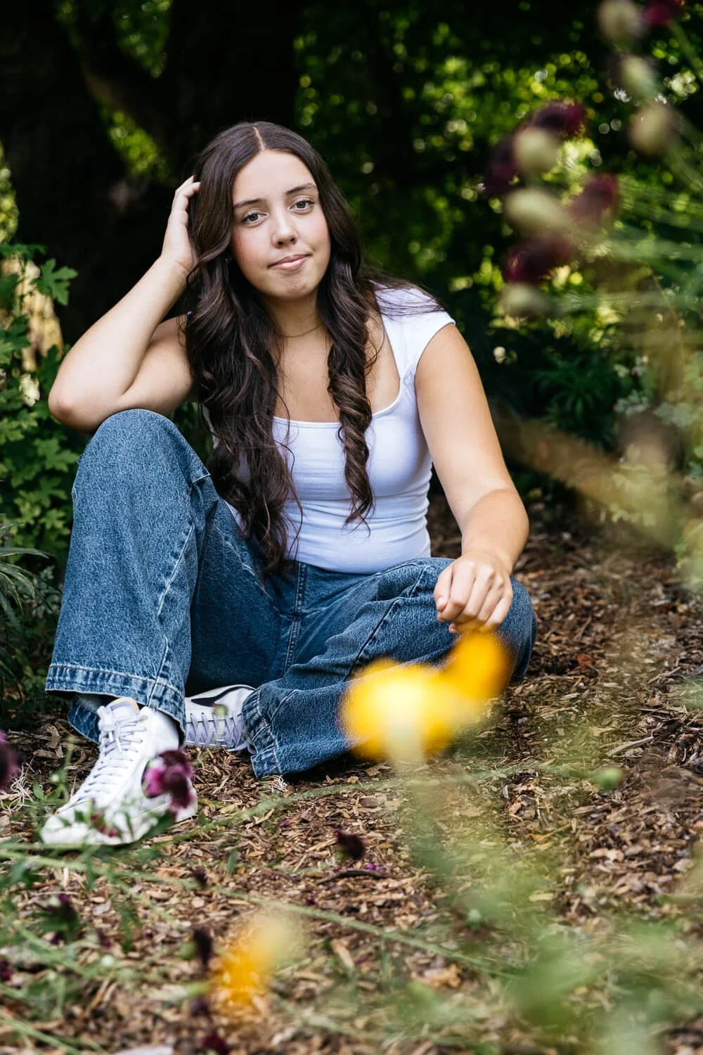 Teen with long brown hair sits amongst flowers at Blake Garden in Kensington.