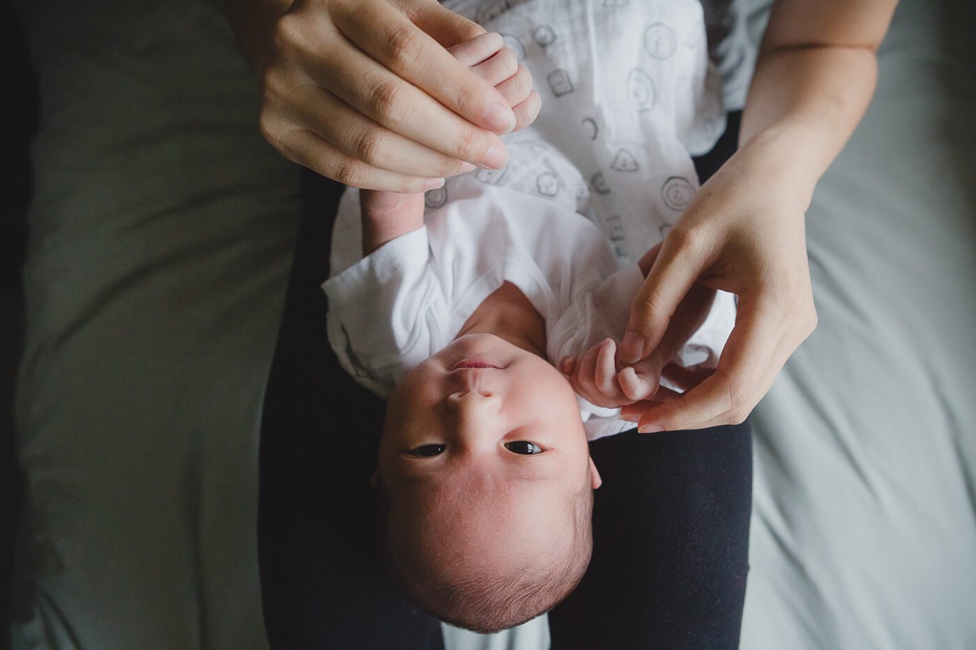 Newborn on mom's lap looks up at camera while mom hold baby's hands.