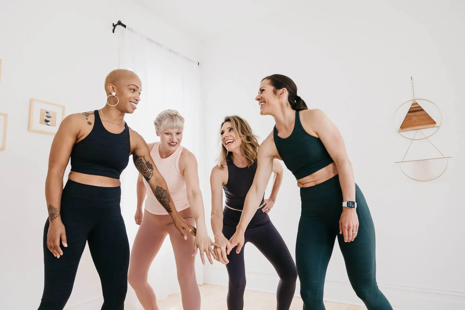 Four women in active wear give low fives while laughing in white walled room, shot for Every Mother in San Francisco.