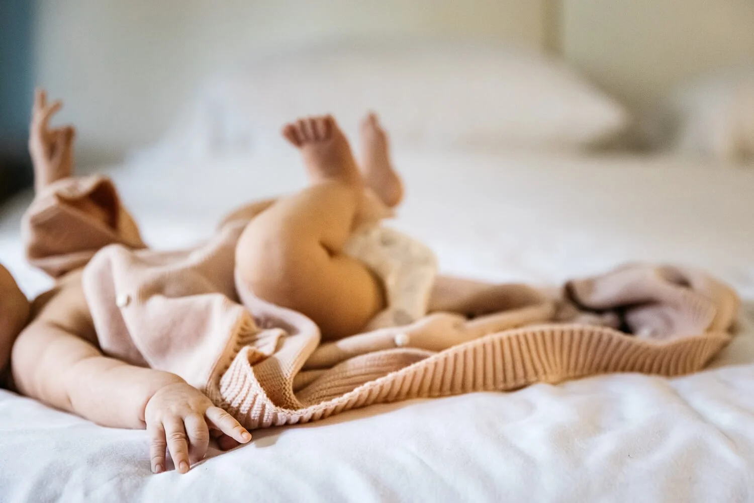 Crop of newborn baby's arms and legs on a bed, with pink blanket wrapped around.