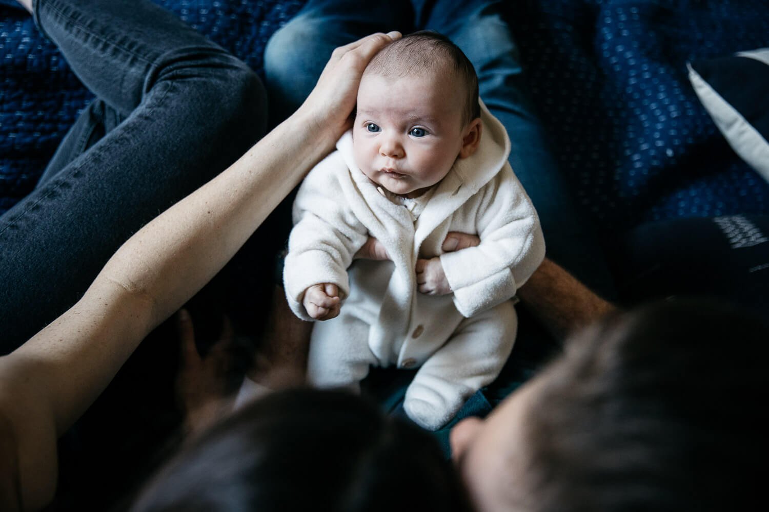 Birdseye view of parents arms holding newborn wearing cozy white hooded pajamas.