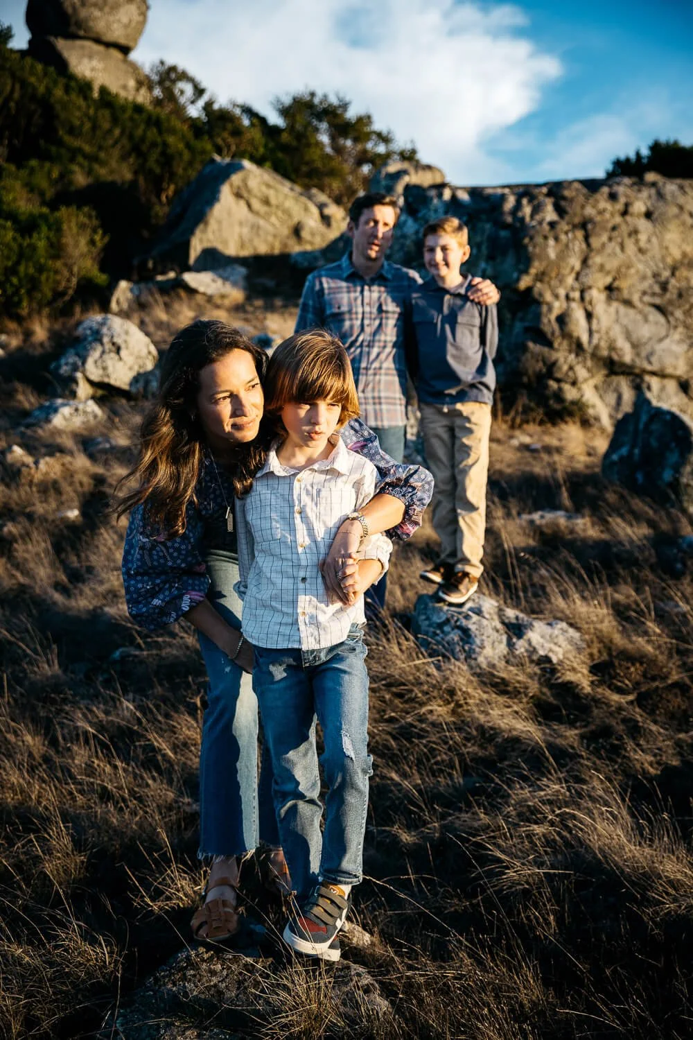 Mom stands with young son on boulder at Ring Mountain, while warm sunset light falls on them.