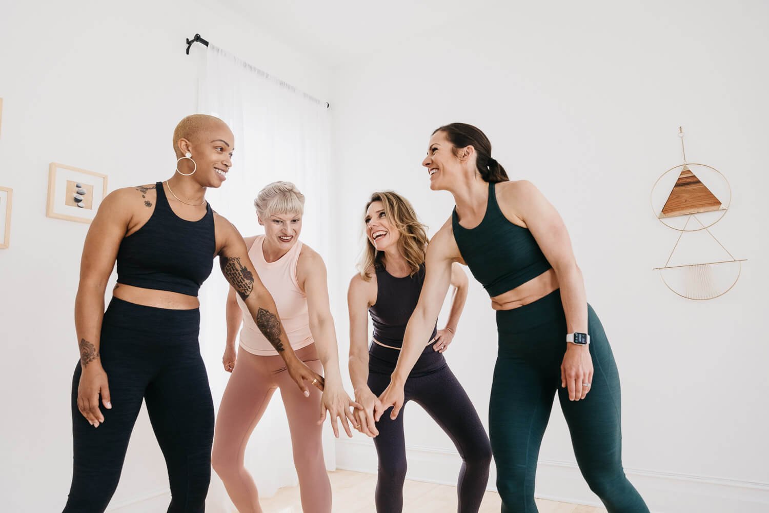 Every Mother fitness team stands in semi-circle and smiles at each other in bright, white room.