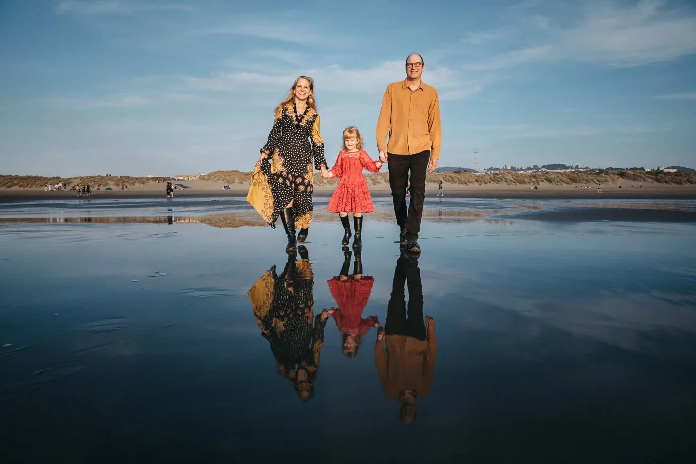 Family of three walks in the surf at Ocean Beach, their reflections in the glassy wet sand.