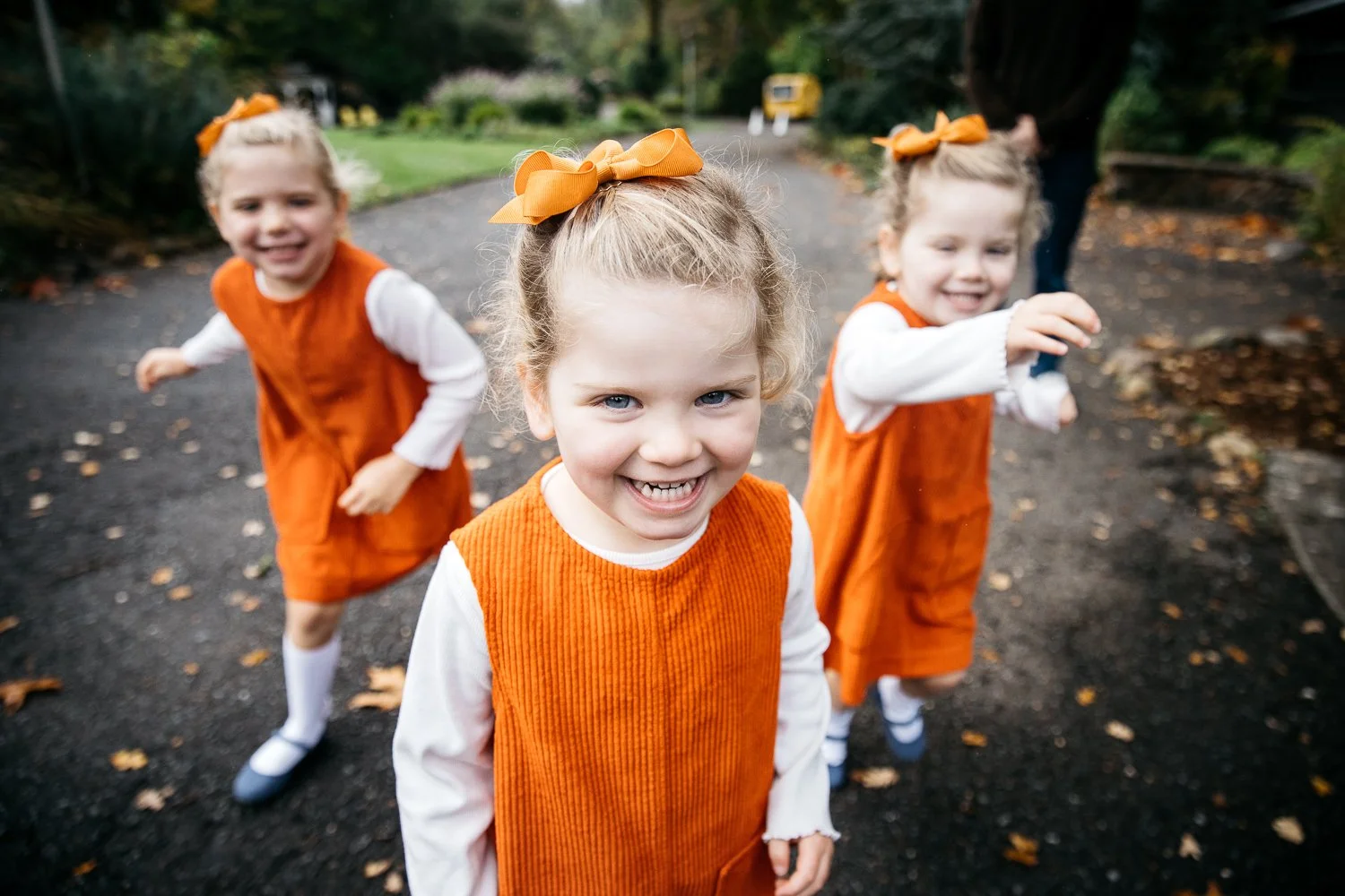 Three sisters in orange pinafore dresses laugh at the Marin Art and Garden Center. 