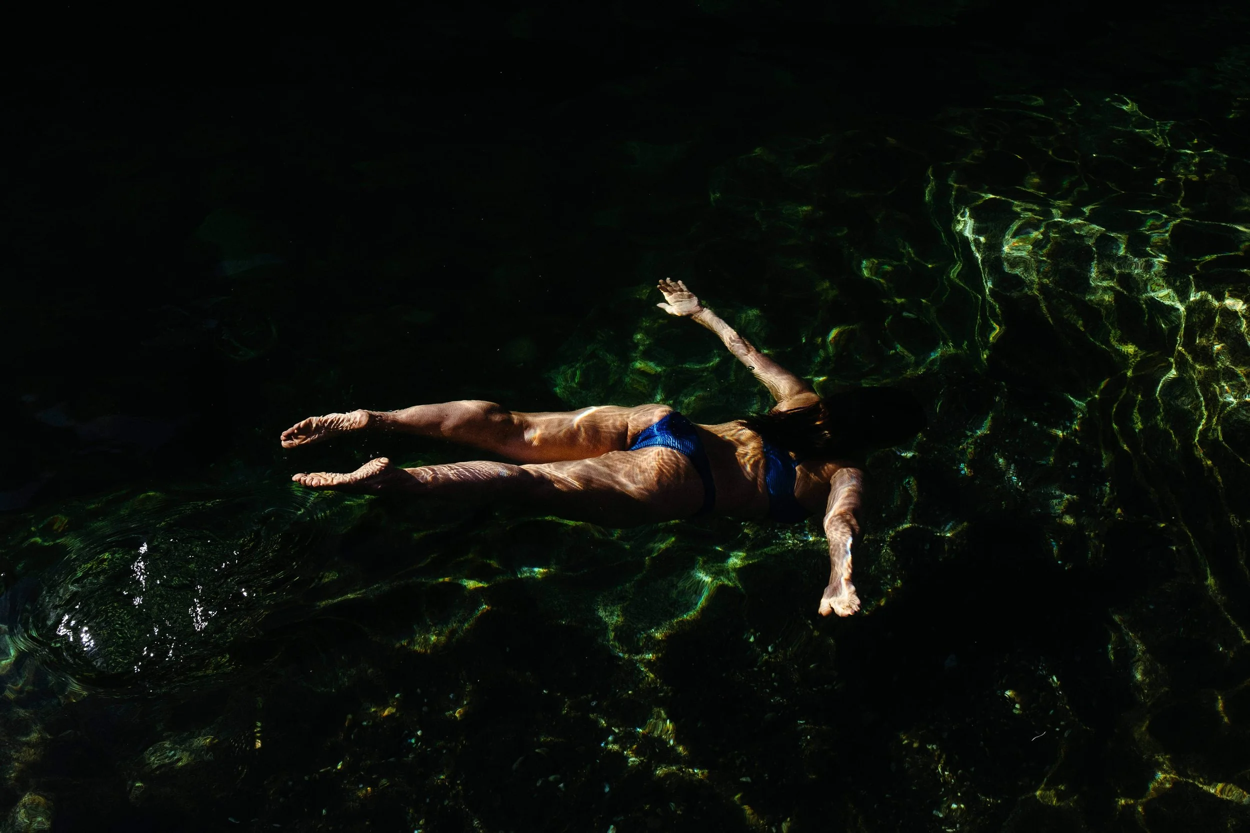 Woman in bright blue bikini swims under the surface of the water, shot at the Yuba River.