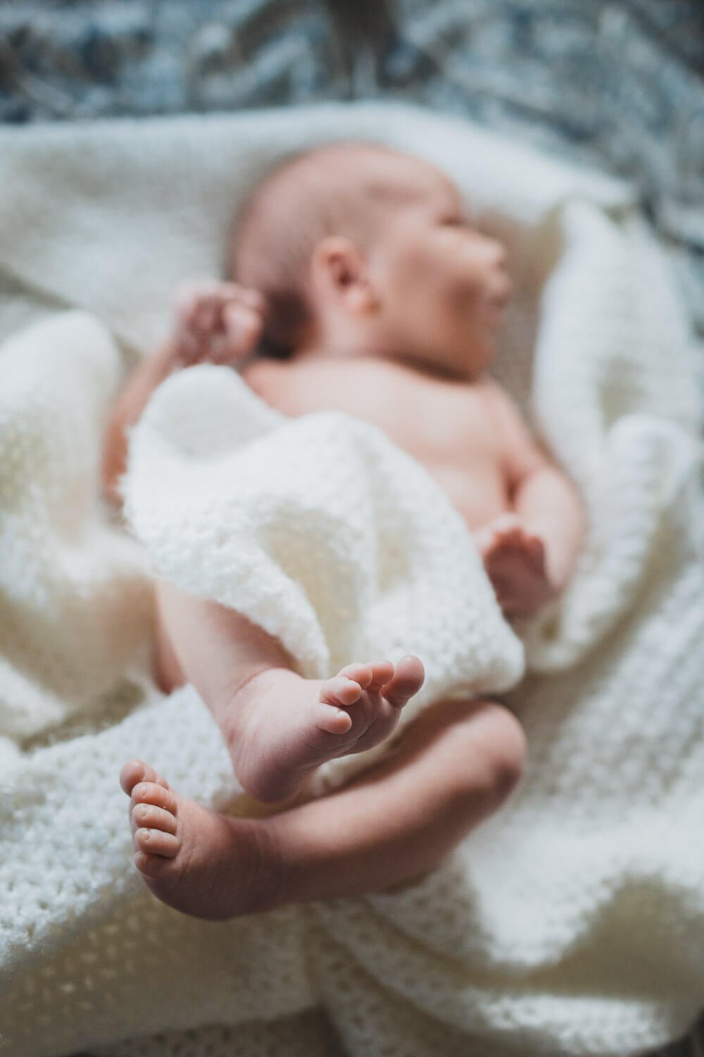 Newborn toes in focus while rest of baby in soft focus and wrapped in cosy white blanket.
