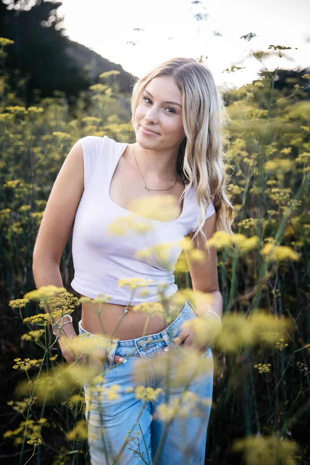 Blond teen girl stands surrounded by tall yellow flowers, shot during senior photo session in the Marin Headlands.