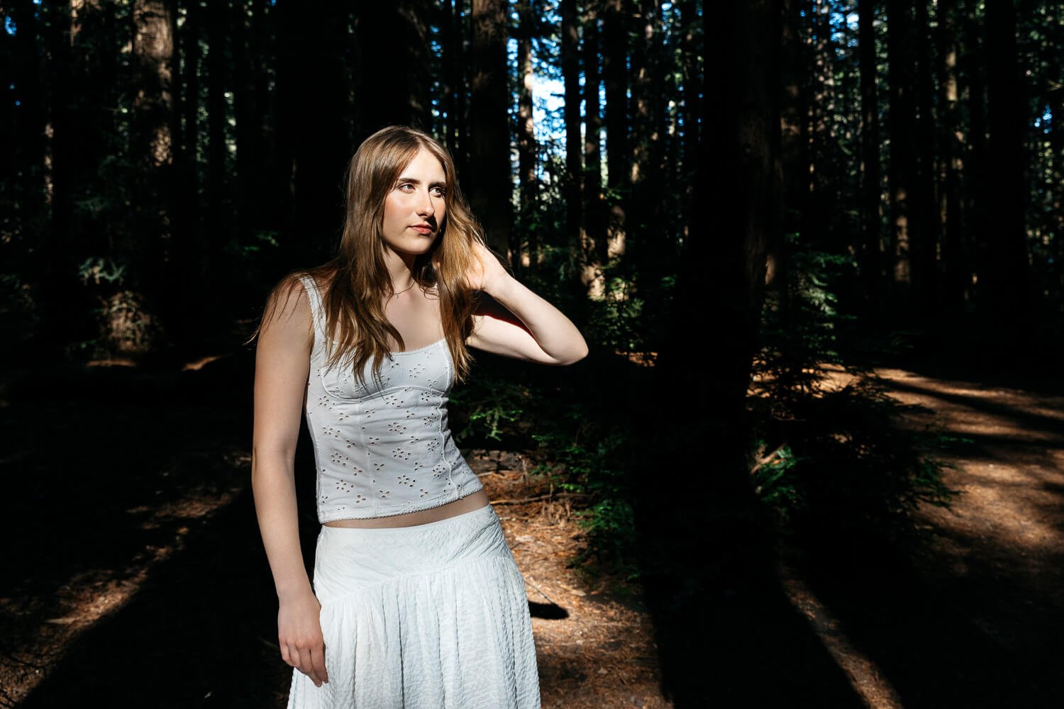 Senior portrait of teen in white tank and skirt, standing light tunnel amongst trees at Redwood Regional in Oakland, CA.