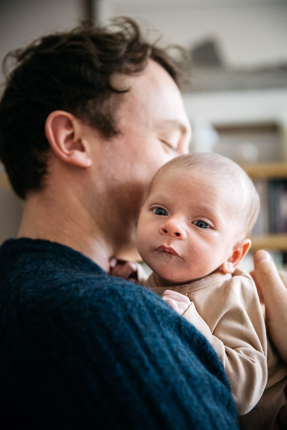 Newborn held by Dad, looking over his shoulder and at the camera.