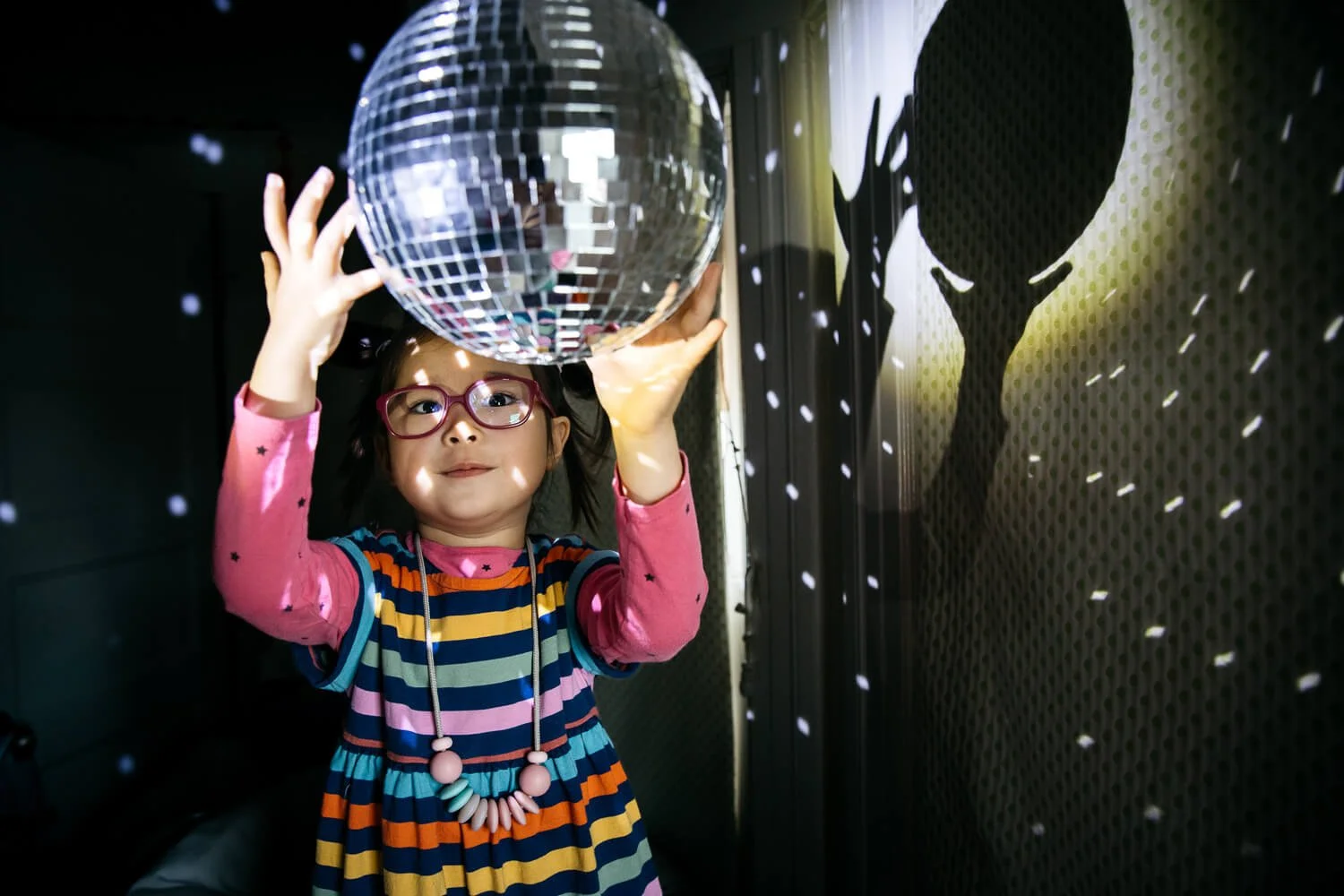 Young girl in striped dress spins mirror ball while light dances around room.