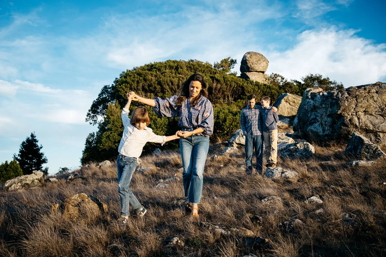 Mom walks boy over trail of boulders at Ring Mountain during sunset family photoshoot.