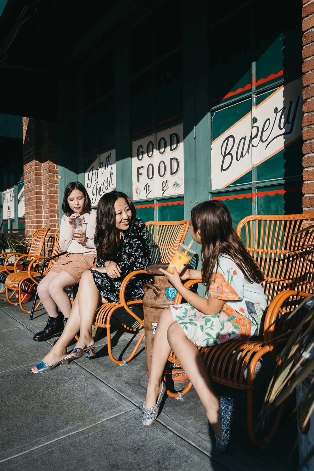 Mom smiles at tween daughters while stead in front of colorful market mural in Alameda.