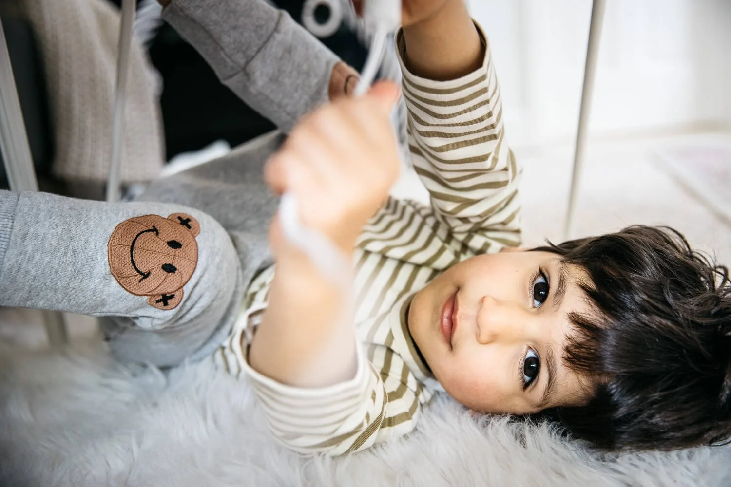 Toddler big brother playing on rug during in-home newborn lifestyle session in San Francisco. He looks into the camera with interest.
