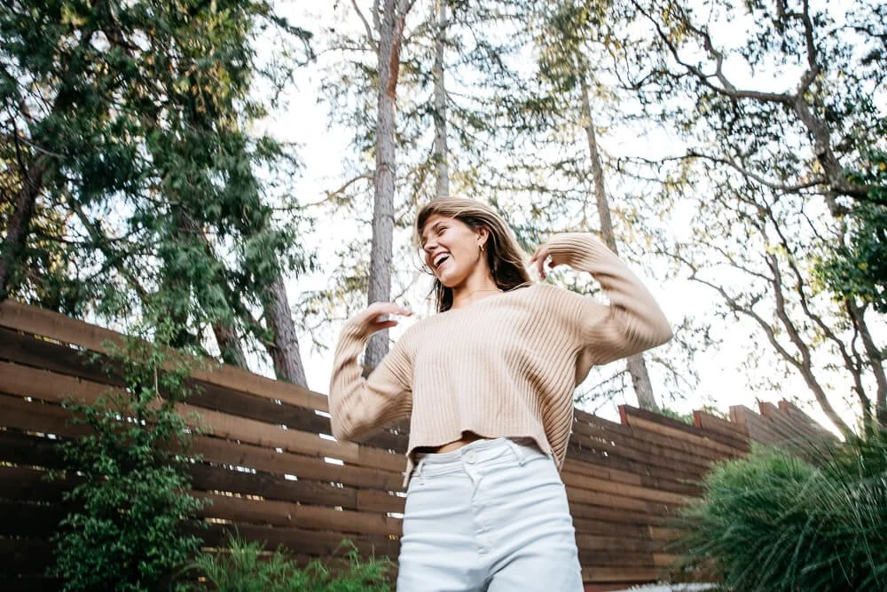 Teen girls laughs and switches her long hair, while standing in her backyard during family photoshoot.