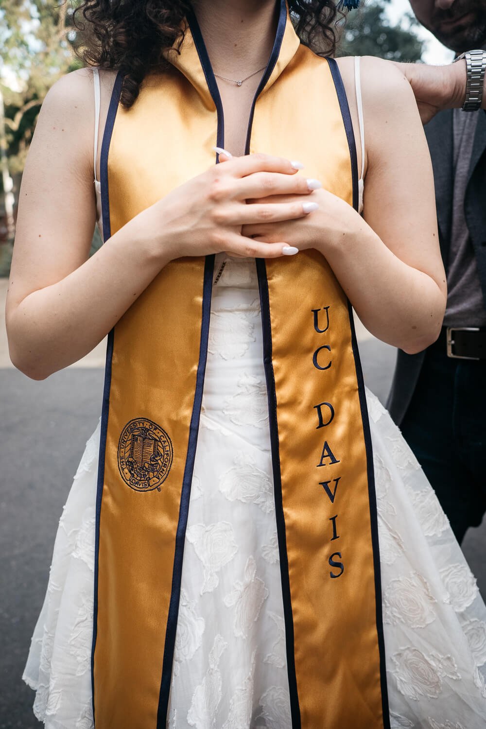 Crop of graduating senior girl crossing her arms in front of her UC Davis graduation sash.