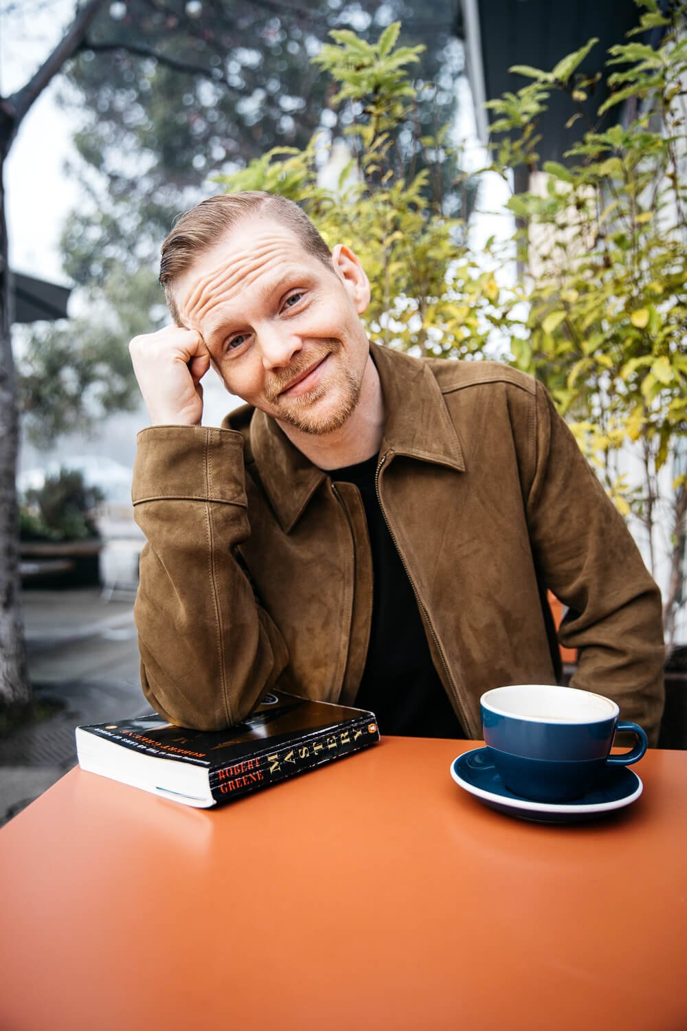 Man sits at orange cafe table for dating portrait with coffee and book.