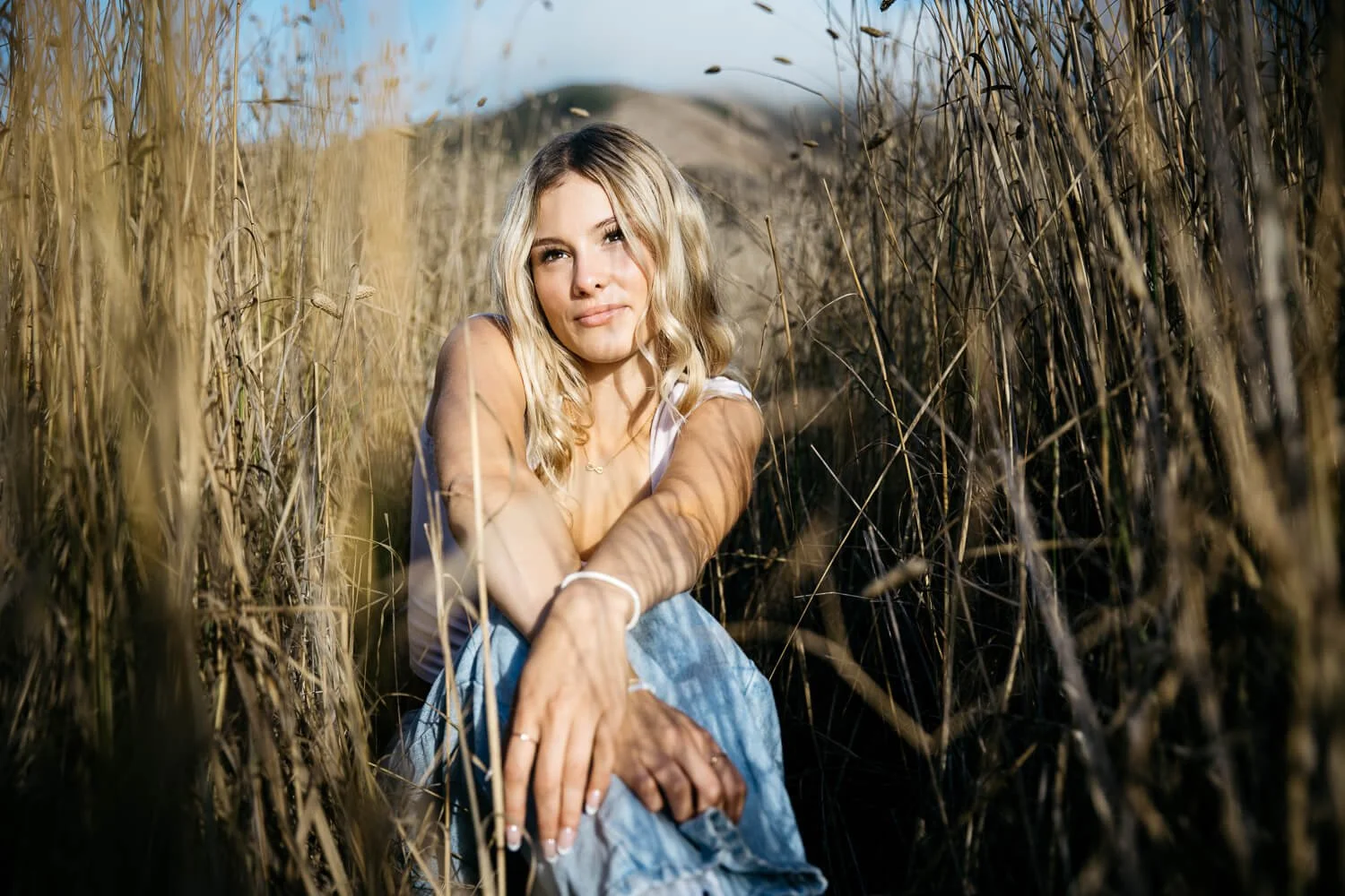 Teen with long blond hair sits in tall grasses during senior session in the Marin Headlands.