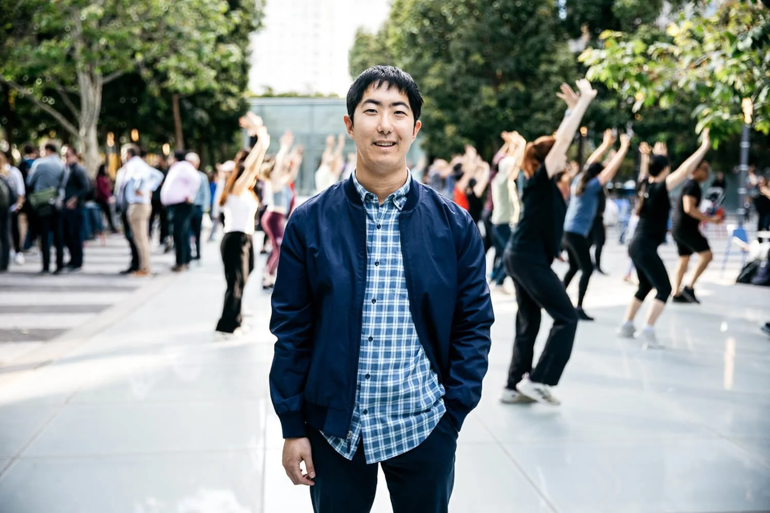 Asian man stands smiling among group doing outdoor dance class, shot at Salesforce Park in San Francisco.