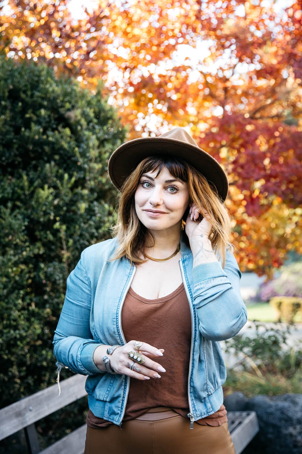 Woman in blue jacket and brown hat stands in front of fall foliage and smiles, shot at Marin Art and Garden Center.