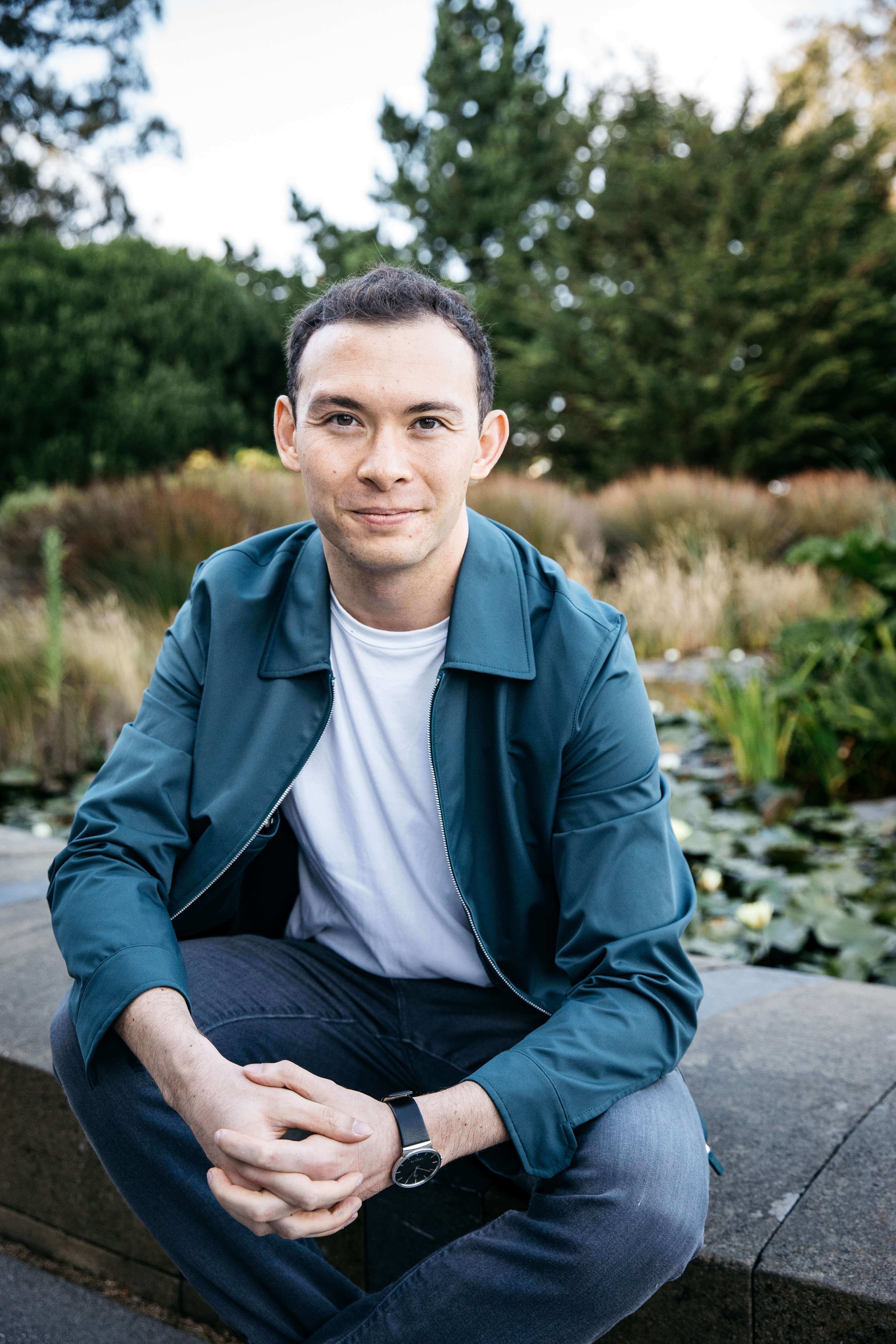 Man in blue jacket and white tee sits at edge of lily pond at the deYoung Museum in Golden Gate Park.