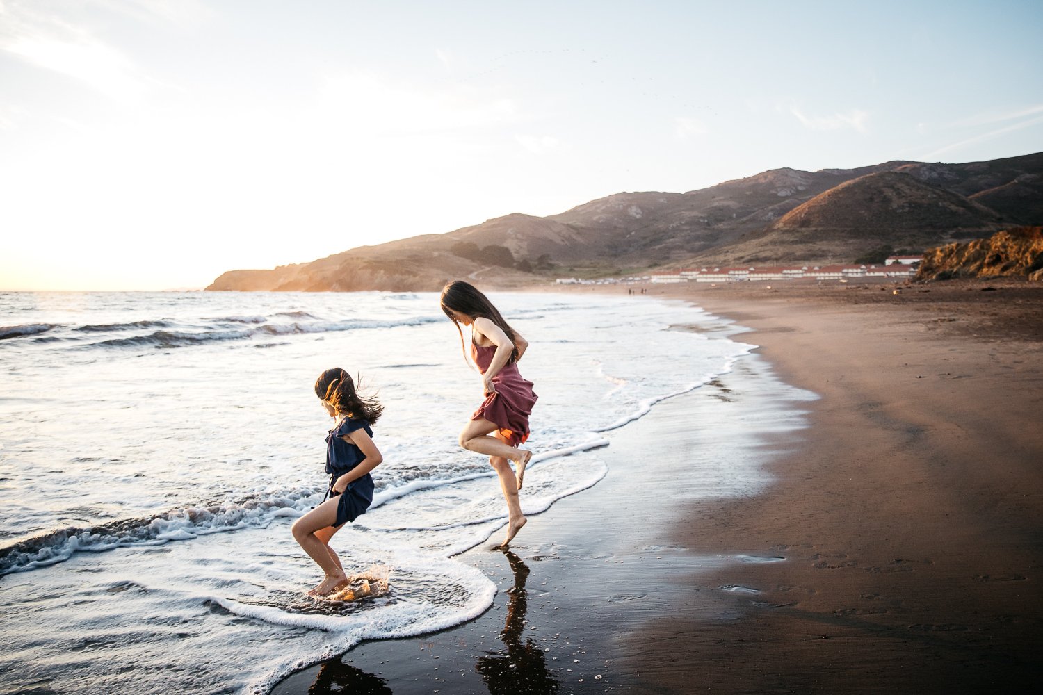 Mom and daughter jump in the surf at Rodeo Beach during family photo shoot in the Marin Headlands.