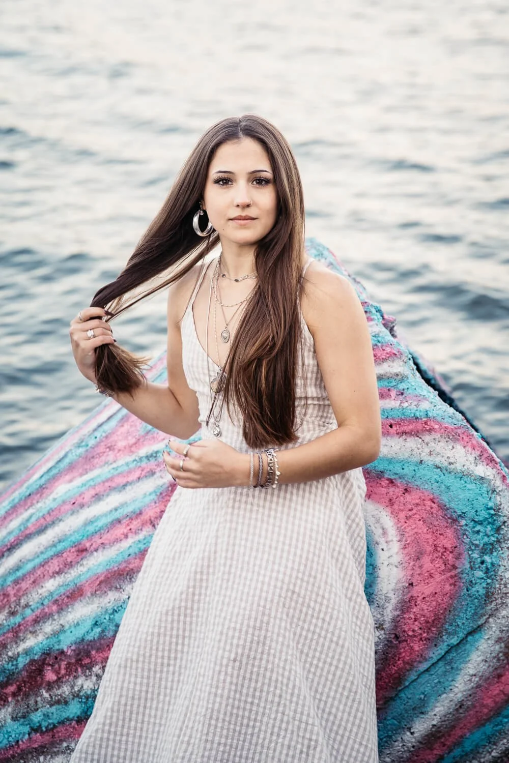 San Francisco senior photographer captures high school senior in a white gingham dress leaning against colorful graffiti wall at the Albany Bulb with the Bay in the background.