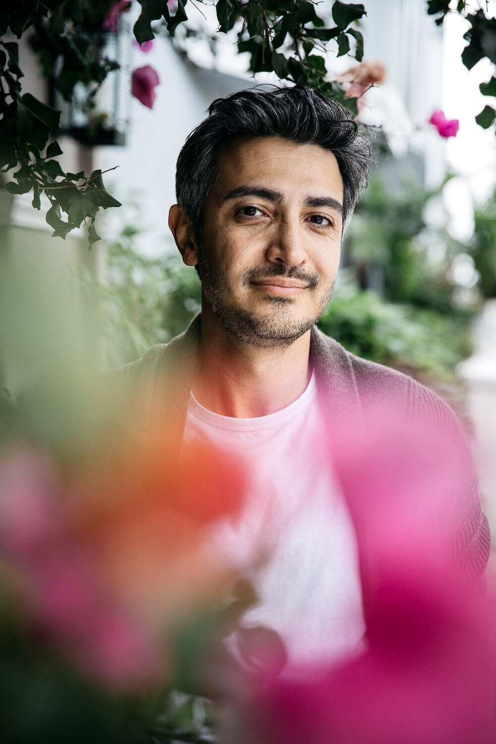 Man with dark hair and cardigan over white tee stands surrounded by pink bougainvillea, shot  on Chestnut Street in San Francisco. 