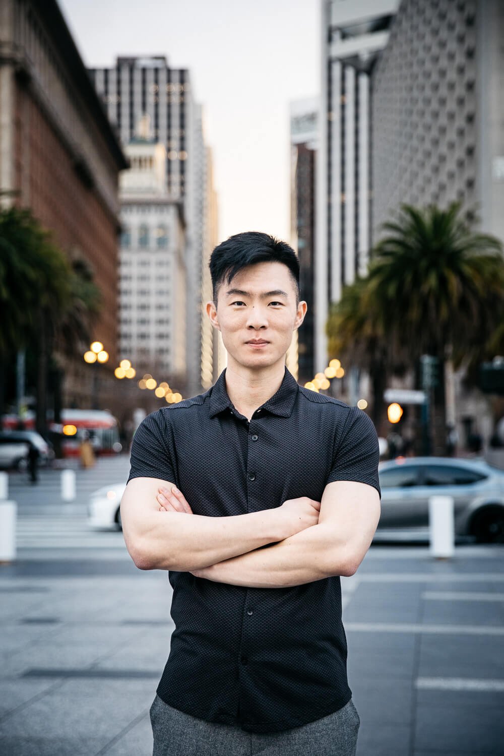 Asian man in black shirt stands with crossed arms and San Francisco downtown skyline in the background.