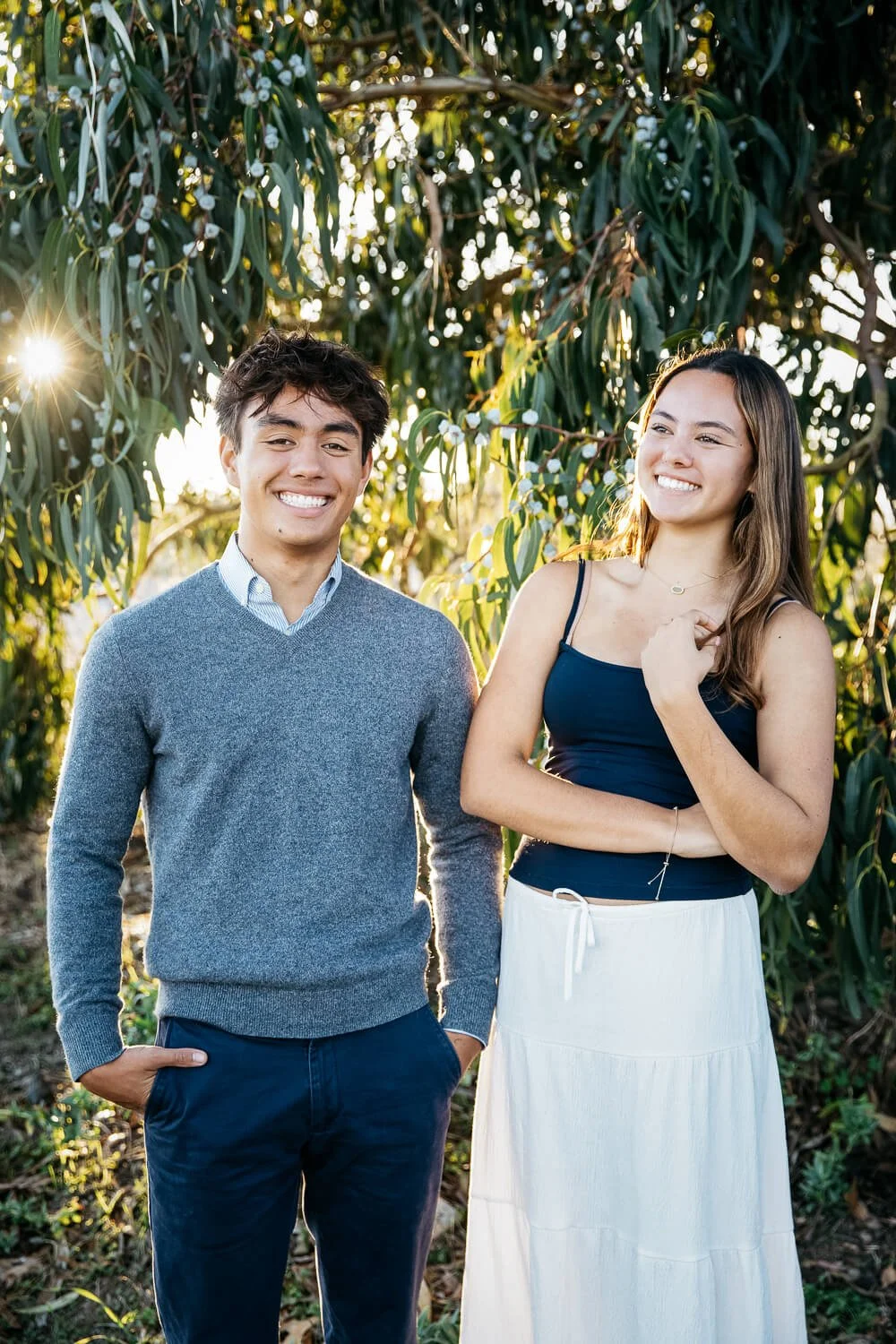 Teen boy-girl siblings stand laughing under  a eucalyptus tree, shot during senior photoshoot at the Albany Bulb.