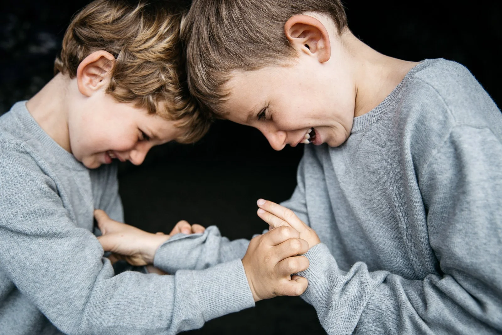 Two brothers play wrestle against a black background during family photo shoot in San Francisco
