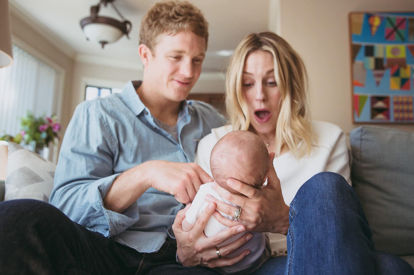 Mom and dad cradle newborn in front of them and marvel at baby.