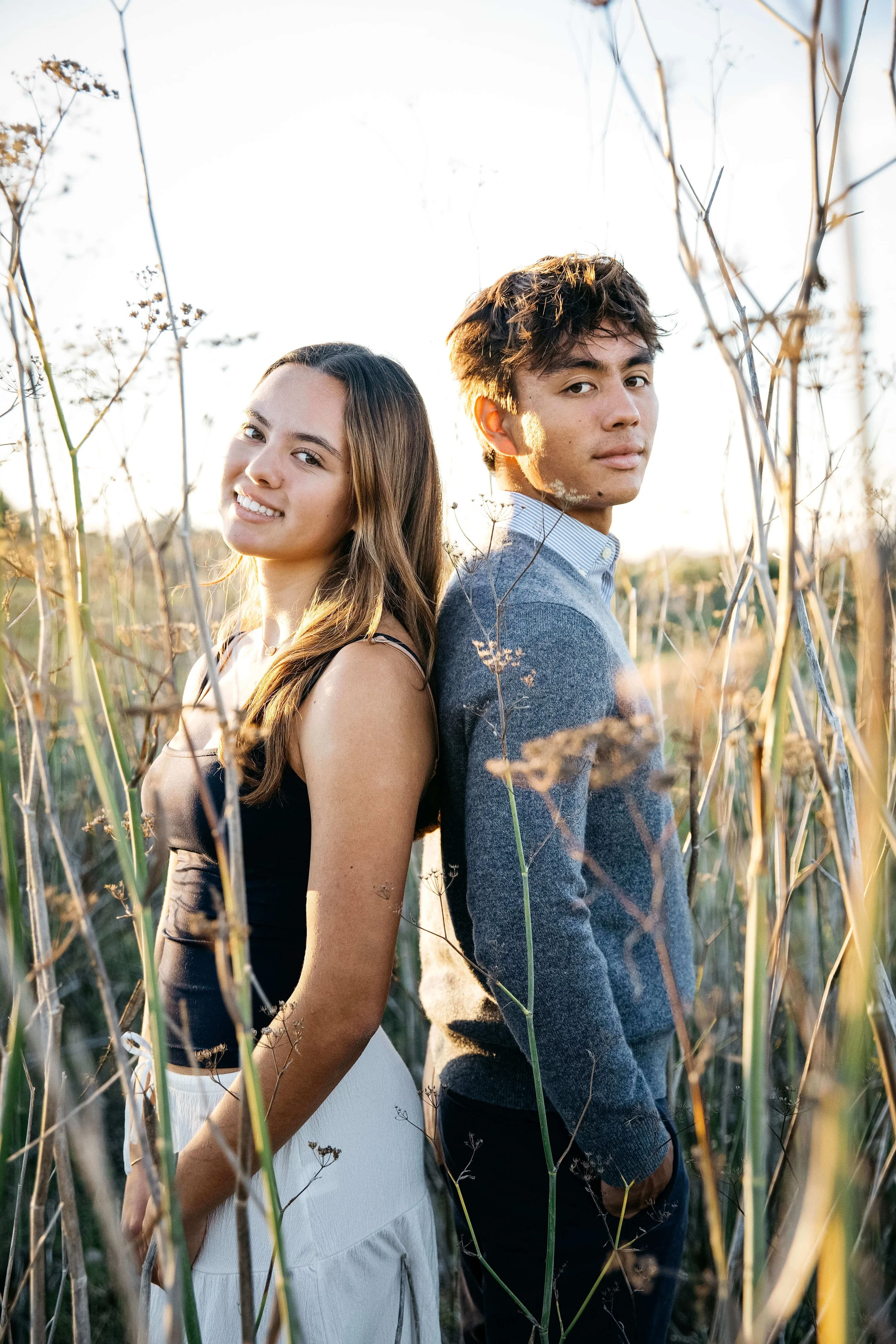 Teen boy-girl siblings stand back-to-back in tall stands of blooming anise, shot during senior photoshoot at the Albany Bulb.