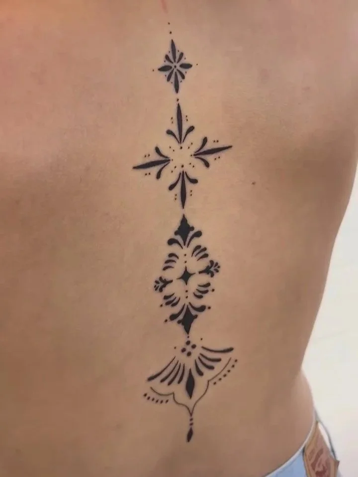 Black decorative tattoo on person's side, consisting of symmetrical floral and geometric patterns arranged in a vertical line.