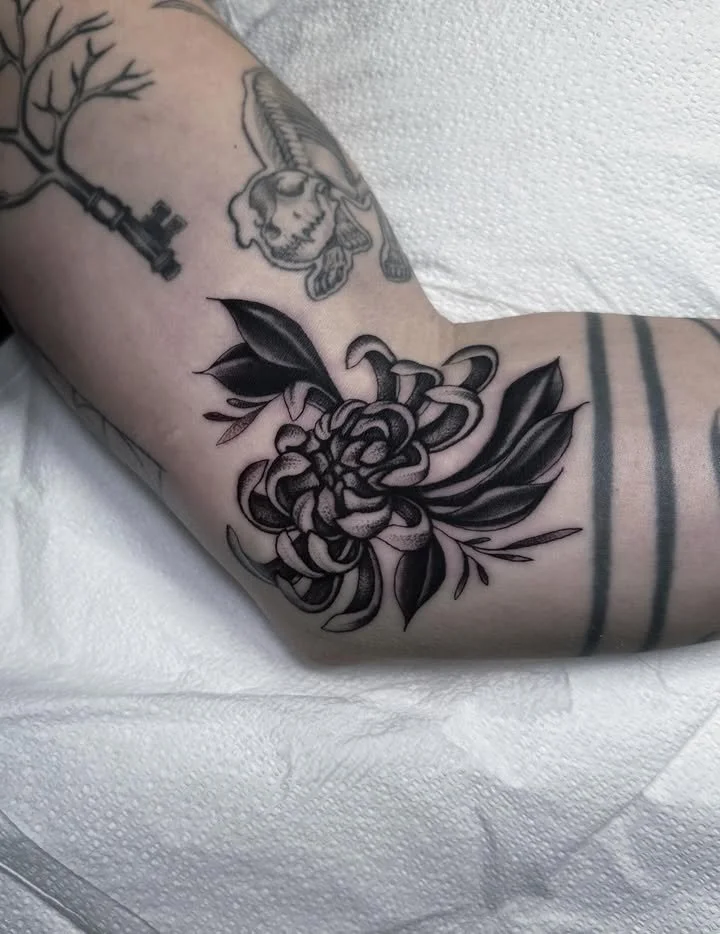 Black and gray tattoo of a peony flower with leaves on a person's arm.