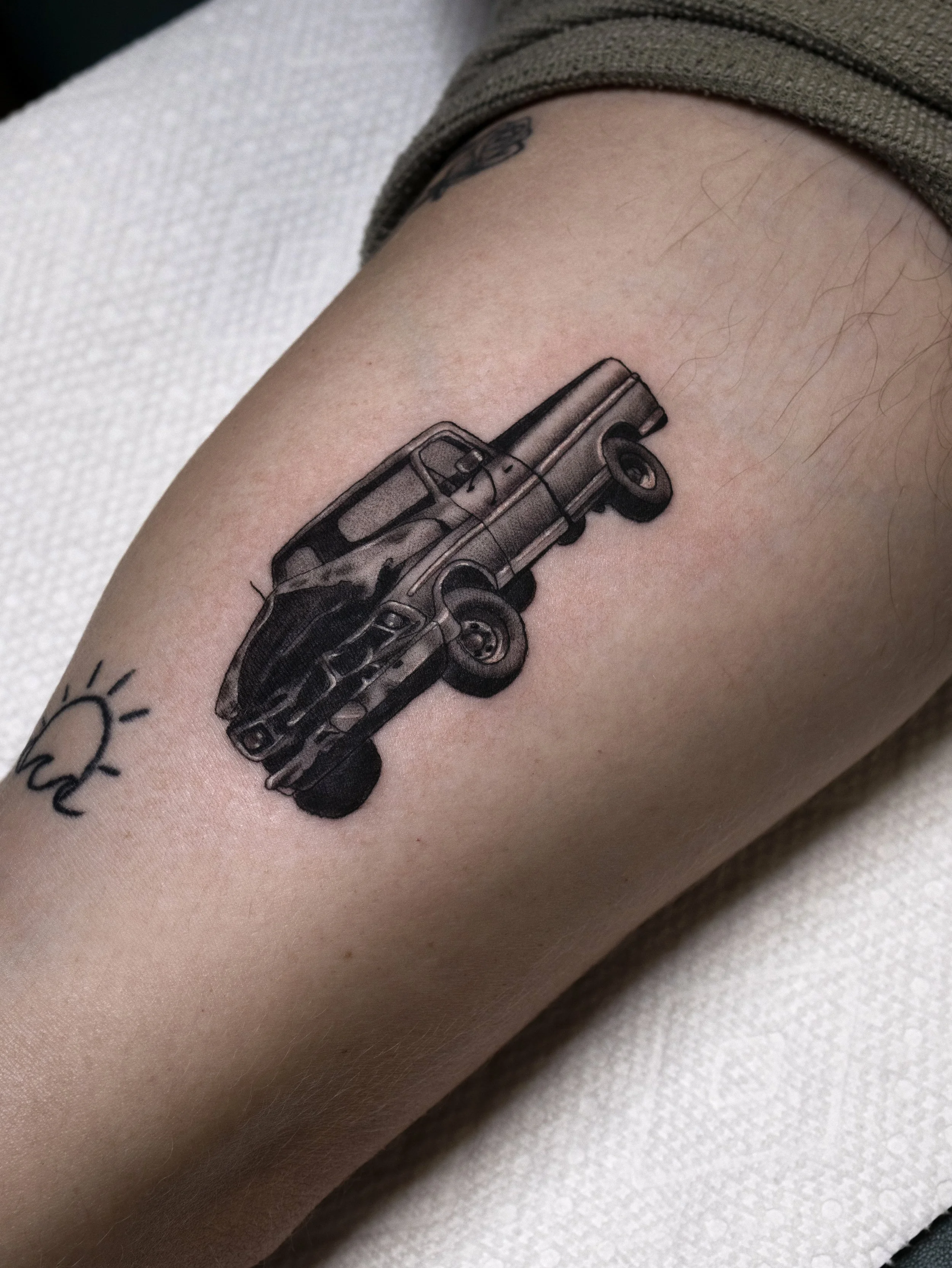 A close-up of a person's upper arm with a tattoo of a detailed black and gray handgun.