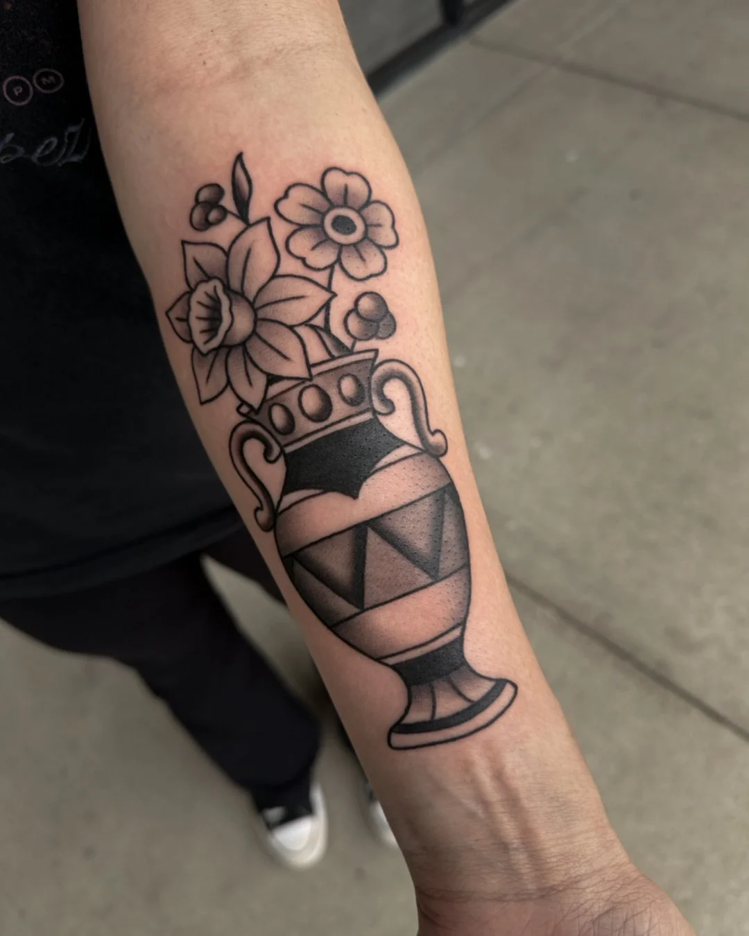 Tattoo of a vase with flowers on a person's forearm.